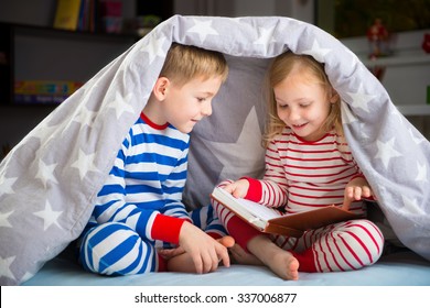 Two happy siblings reading book under the cover