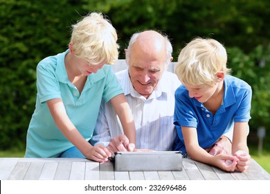 Two happy siblings, twin teenage brothers, spending time together with grandfather, teaching him to use tablet pc, sitting together in the backyard of house on sunny day - Powered by Shutterstock