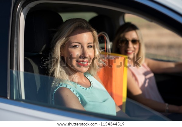 Two happy\
sister in car happy and smiling after shopping, parking in sunny\
summer day with blonde cool\
hairstyle