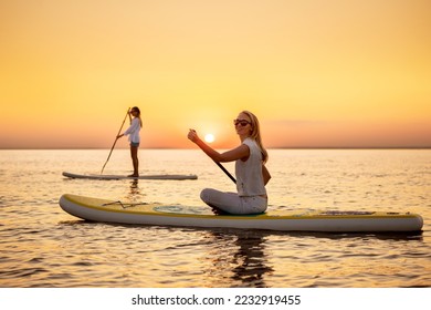 Two happy slim girls are walking on sup stand up paddle boards at sunset calm lake - Powered by Shutterstock