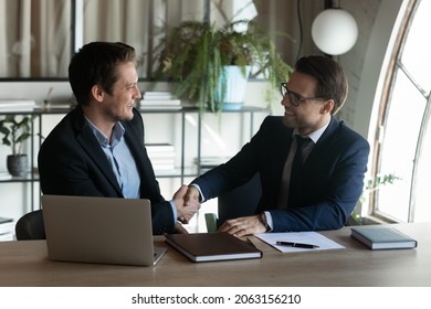 Two happy smiling businessmen shake hands in office after making successful deal. Satisfied young man customer appreciate lawyer banker financial counselor for help assistance good consultation advice