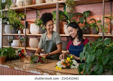 Two happy and smiling young woman florist working together in flower shop. Florist talking and making beautiful bouquet of flower together with her black colleague. Beautiful florists arranging bunch. - Shutterstock ID 2141412461
