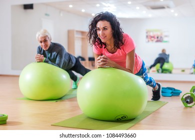 Two Happy Sportswomen Exercising With A Swiss Ball Doing Plank Exercise In Gym