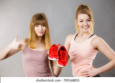 Two happy sporty smiling women presenting sportswear trainers red shoes, comfortable footwear perfect for workout and training.
