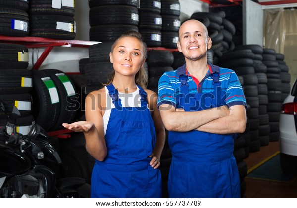 two happy technicians in coveralls standing at car\
service point