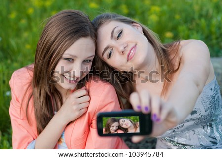 Two happy teenage girls taking selfshot or selfy picture of themselves with mobile phone portrait