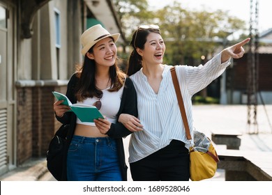 Two happy tourists female friends travel in summer vacations with guide book. group of cheerful sisters walking under sunset time with sun flare. lady point finger showing view and smiling joyful.