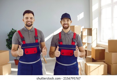 Two happy truck delivery or moving company workers guarantee best service. Portrait of young men in uniform workwear standing in living room or office, looking at camera, showing thumbs up and smiling - Powered by Shutterstock