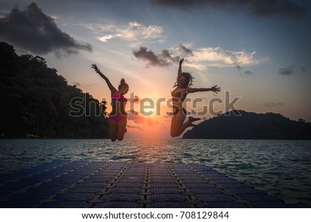 Two happy woman in bikini jumping on seafloat in the sea beach at sunset time, Andaman sea, Mu Koh Surin island, Phangnga, Thailand