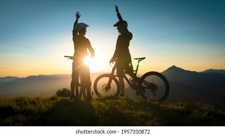 Two happy woman high five over the sunset after a successful mountain biking trip in the mountains. Celebrate a cross country cycling journey. - Powered by Shutterstock