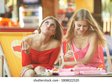 Two happy women eating sushi rolls. Blurred background. - Powered by Shutterstock