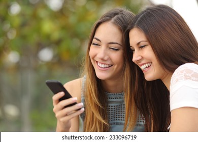 Two happy women friends sharing social media in a smart phone outdoors in a park