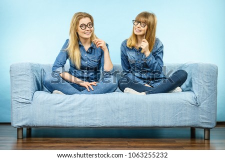 Two happy women holding fake eyeglasses on stick having fun fooling around wearing jeans shirts. Photo and carnival funny accessories concept.
