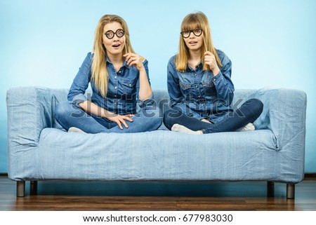 Two happy women holding fake eyeglasses on stick having fun fooling around wearing jeans shirts. Photo and carnival funny accessories concept.