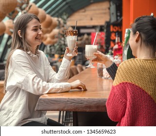 Two Happy Women Are Sitting In A Cafe, Drinking Milkshakes, Telling Each Other Funny Stories, Being In A Good Mood, Laughing Happily. Best Friends Have Fun Together In The Cafe