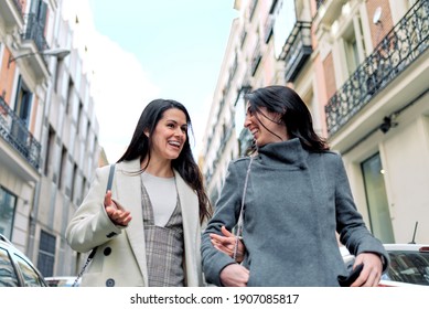 Two happy women talking and walking in the street.
