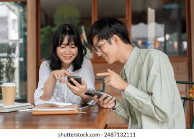 Two happy young Asian friends are enjoying talking while watching a video on a smartphone together, relaxing at a coffee shop in the city. people, lifestyle, and wireless technology - Powered by Shutterstock