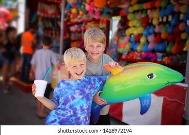 Two Happy Young Boy Children Are Smiling With Their Slushie And Toy Prize A A Small Town American Carnival.