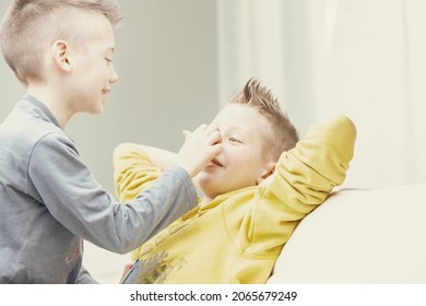 Two Happy Young Brothers Enjoying Playing Together Indoors On A Sofa In The Living Room In A Close Up High Key Portrait