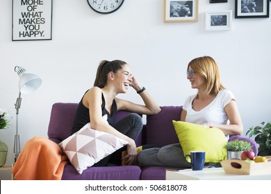 Two Happy Young Female Friends Conversing In The Living Room At Home