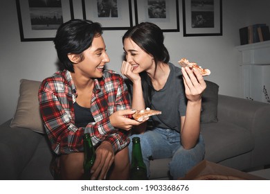 Two happy young girls laughing, drinking beer, sharing pizza at home party late. Cheerful best friends or couple talking, having fun enjoying eating fast food at night sitting on couch together. - Powered by Shutterstock