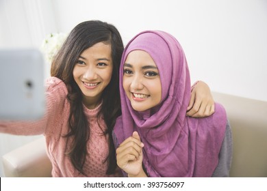 two happy young muslim woman take self portrait with handphone at home