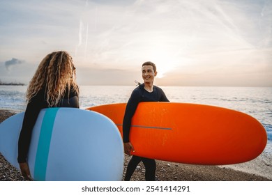 Two happy young surfers with surfboard prepares to hit the waves at sunset. Sports active vacation - Powered by Shutterstock