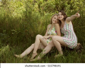 Two happy young woman friends siting on grass in forest
