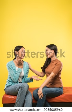 two happy young women chatting and joking while sitting on the sofa