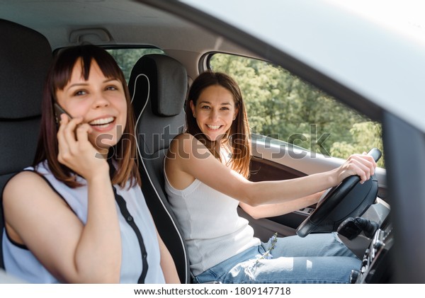 Two happy young women\
friends are driving a car and enjoy the company. Travel with you\
friend concept