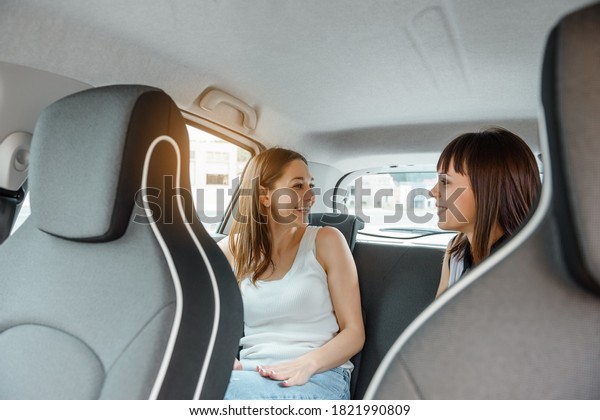Two happy young women friends are talking to each\
other in the car at rear seat and enjoy the company. Travel with\
you friend concept
