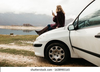 Two happy young women on car trip. They are having fun while one is sitting on the car and one with hijab is near window. They are smiling and enjoying their time together.