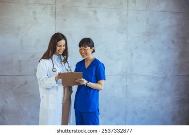 Two healthcare professionals collaborate in a modern hospital setting, smiling while discussing patient information. The image portrays teamwork, professionalism, and a positive medical environment. - Powered by Shutterstock