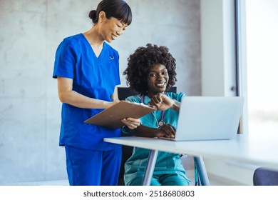 Two healthcare professionals discuss patient information using a laptop and clipboard in a bright office. They demonstrate teamwork and communication in a clinical setting. - Powered by Shutterstock