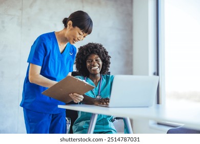 Two healthcare professionals discussing patient records in a bright office. One holds a clipboard, while the other engages with a laptop, reflecting teamwork and communication. - Powered by Shutterstock