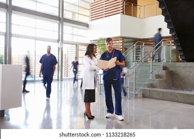 Two healthcare workers talk in the lobby of a busy hospital