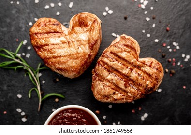 
two heart shaped grilled pork steaks with spices for valentines day on stone background. dinner concept for two for valentines day celebration