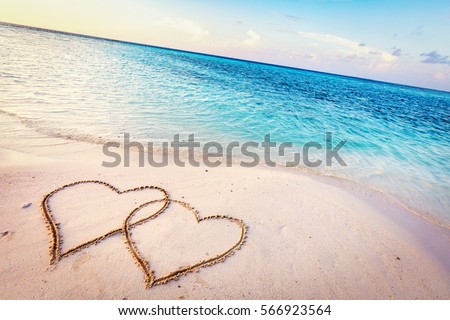 Two hearts drawn on sand of a tropical beach at sunset. Clear turquoise ocean. Maldives islands.