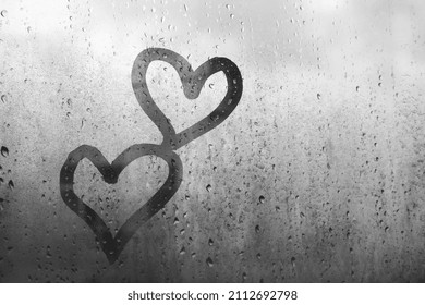 Two hearts drawn on window glass by finger, black and white, fogged with raindrops - Shutterstock ID 2112692798