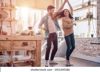 Two hearts filled with love. Full length of beautiful young couple in casual clothing dancing and smiling while standing in the kitchen at home