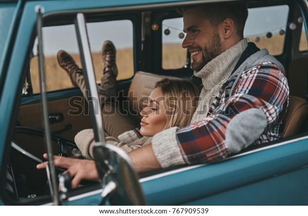 Two hearts full of love. Attractive young woman\
resting in her boyfriend?s arms while traveling in retro style mini\
van