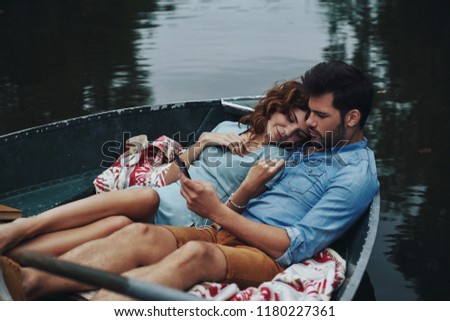 Two hearts full of love. Beautiful young couple listening music while sitting in the boat outdoors