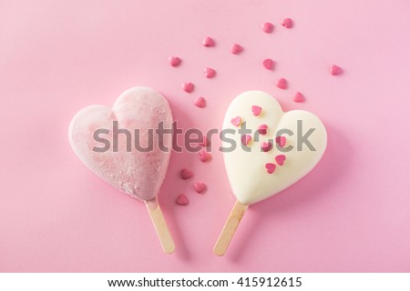 Two heart-shaped ice cream covered with confetti on pink background