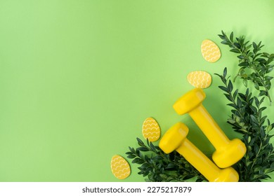 Two heavy dumbbells, boxwood branches and decorative Easter eggs. Healthy fitness lifestyle composition, gym workout and training concept. Fit flat lay with copy space on green background. - Powered by Shutterstock