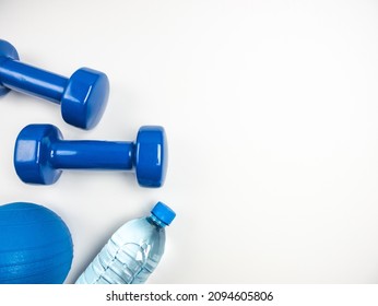 Two heavy dumbbells for workout, plastic bottle of water and a small exercise pilates ball. Healthy fitness lifestyle composition. Gym flat lay concept with copy space on white background.