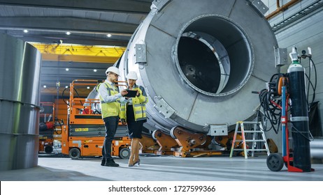 Two Heavy Industry Engineers Stand in Pipe Manufacturing Factory, Use Digital Tablet Computer, Have Discussion. Facility for Construction of Oil, Gas and Fuel Pipeline Transportation Products - Powered by Shutterstock