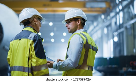 Two Heavy Industry Engineers Stand in Pipe Manufacturing Factory, Use Digital Tablet Computer, Have Discussion. Construction of Oil, Gas and Fuels Transport Pipeline. Back View Sparks Flying - Shutterstock ID 1727599426