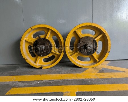 Two heavy-duty yellow elevator traction sheaves with a rusted central axle, placed on a concrete workshop floor marked with yellow safety lines.