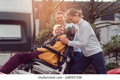 Two helpers picking up disabled senior woman in wheelchair for transport