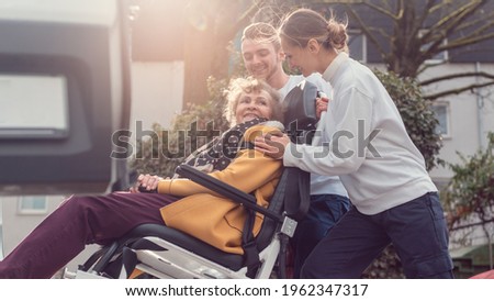 Two helpers picking up disabled senior woman for transport